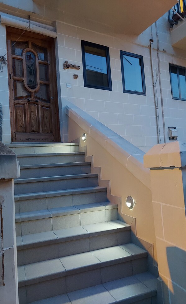 A staircase leading to a wooden door with a glass panel, a small window, and a sign with the number 76. - Gizimina Masionette in Marsascala by the Sea and near Airport (Marsaskala)