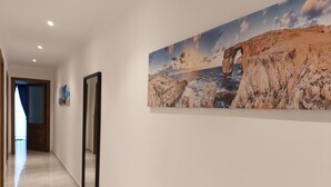 Ein Flur mit einem großen Gemälde einer Küstenlandschaft, einem Spiegel und einer Tür zu einem weiteren Zimmer.