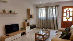 Ein modernes Wohnzimmer mit Flachbildfernseher, Holzmöbeln, einem Glastisch und einem beigefarbenen Sofa.