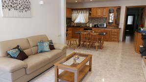 Ein Wohnzimmer mit einem beigefarbenen Sofa, einem Holztisch und einem Essbereich mit Holzsesseln und einem Tisch.