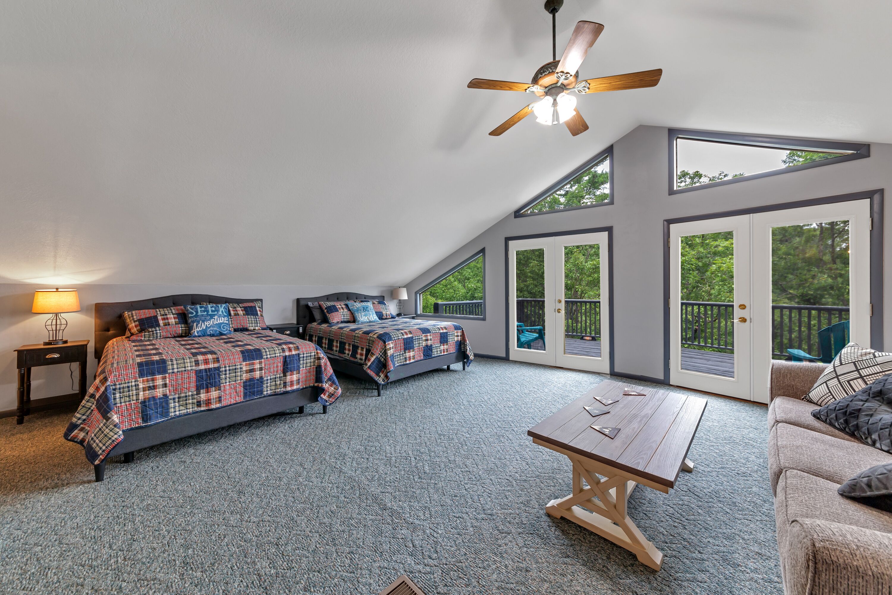 A bedroom with two beds, a ceiling fan, a table, and large windows.