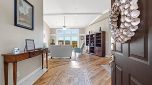 A spacious living room with hardwood flooring, a large window, a sofa, and a decorative shell wall hanging. - Lake View Home with Game Room - Pet Friendly - Spacious Home (Hot Springs)