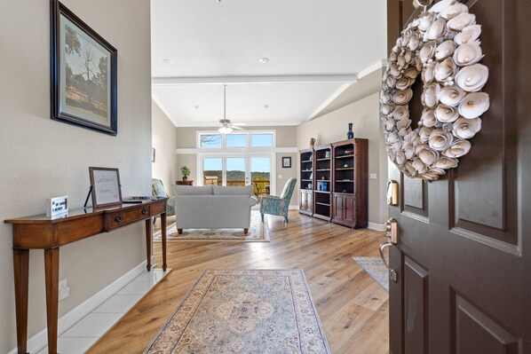A spacious living room with hardwood flooring, a large window, a sofa, and a decorative shell wall hanging.