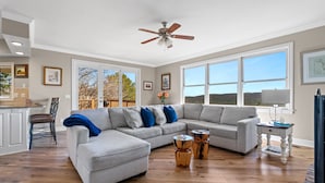 A spacious living room with a large gray sectional sofa, wooden coffee table, and a ceiling fan. - Lake View Home with Game Room - Pet Friendly - Spacious Home (Hot Springs)