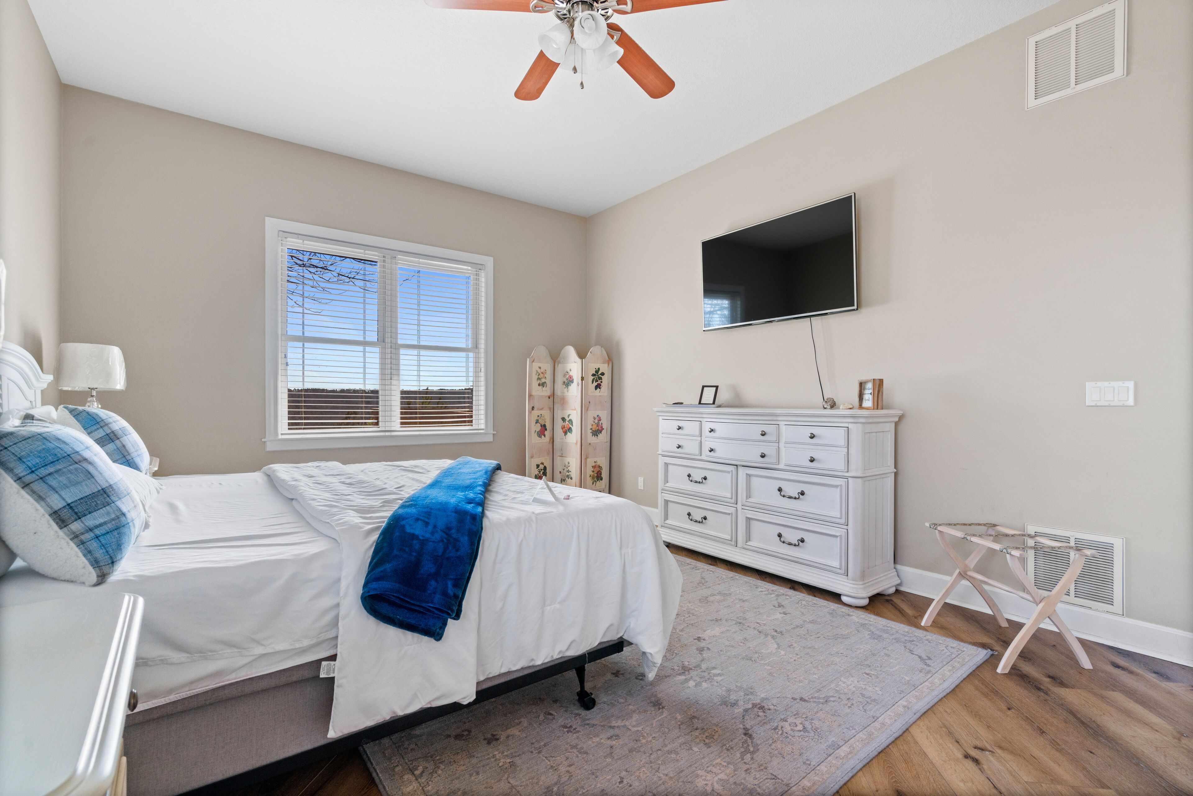 Une chambre à coucher comprenant un lit, une commode, un téléviseur et un ventilateur de plafond.