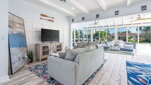Un salon spacieux avec un grand canapé gris, un téléviseur à écran plat et un meuble en bois. Une grande fenêtre offre une vue sur l’extérieur.