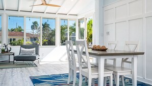 Une pièce spacieuse comprenant un coin repas, un ventilateur de plafond, de grandes fenêtres et une vue sur les palmiers.