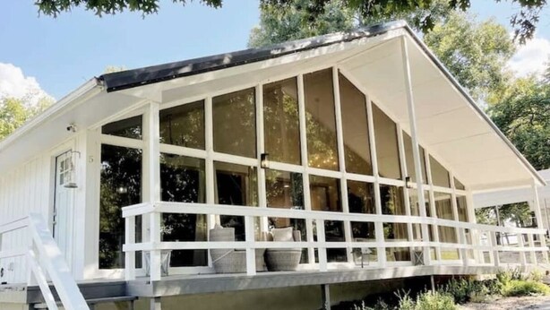Une cabane dotée d’un porche couvert, de grandes fenêtres et d’un escalier menant à l’entrée.