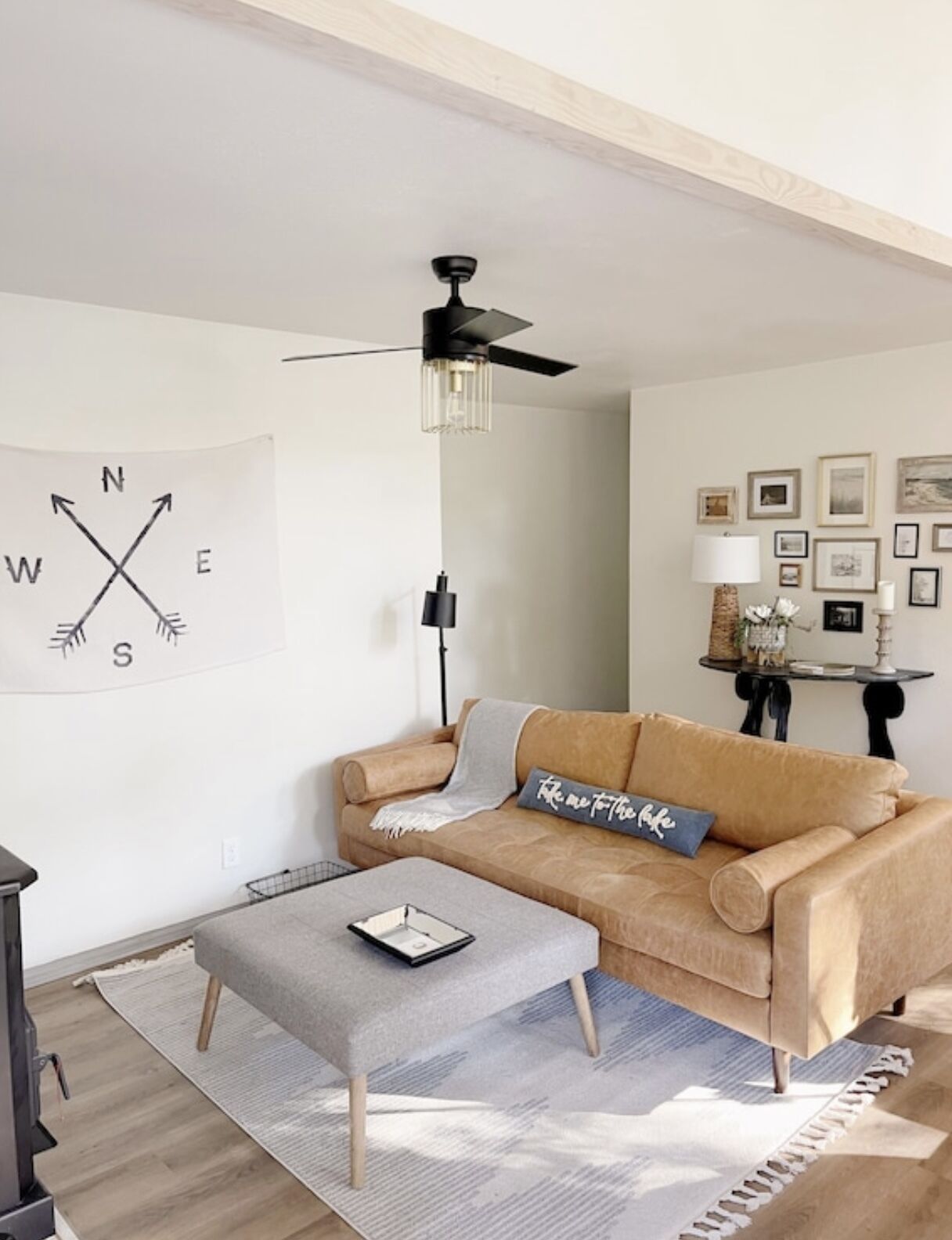 A living room with a beige sofa, a coffee table, a ceiling fan, and wall art including a compass and framed pictures.