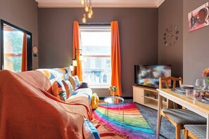 A cozy living room with a bed, a TV, a dining table, and a colorful rug. - Art-Filled Bohemian Apt Colourful Praise Inn (Kingston upon Hull)