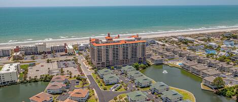 A coastal residential area with a large hotel featuring multiple floors and a distinctive orange roof, surrounded by smaller houses and a body of water.