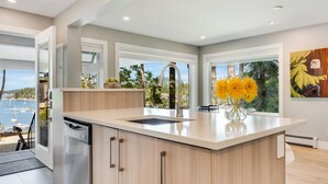 Une cuisine moderne dotée d’un grand îlot central, d’un lave-vaisselle encastré et offrant une vue sur la mer.