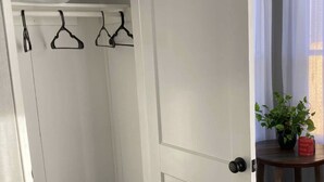 A white closet with three black hangers, a potted plant, and a red candle on a wooden table. - Quiet and Cozy Cottage -10 minutes from the beach! (Corpus Christi)