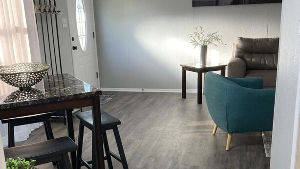 A modern living room with a grey wall, a dining area with a table and chairs, a teal armchair, and a small green plant. - Quiet and Cozy Cottage -10 minutes from the beach! (Corpus Christi)