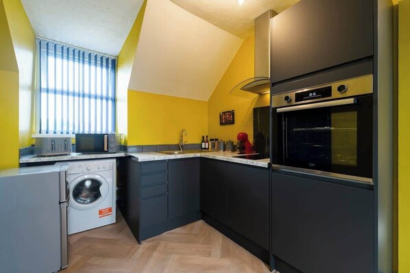 A compact kitchen with a washing machine, oven, and microwave.
