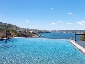 Une piscine d’eau cristalline, d’un bleu éclatant, avec vue sur un lac et des collines lointaines.