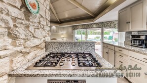 A kitchen with a stone wall, granite countertop, and a gas stove. - Tiger by the Tail Pets OK | Casita & Courtyard Oasis  w/ Heated Pool (Ruidoso Downs)