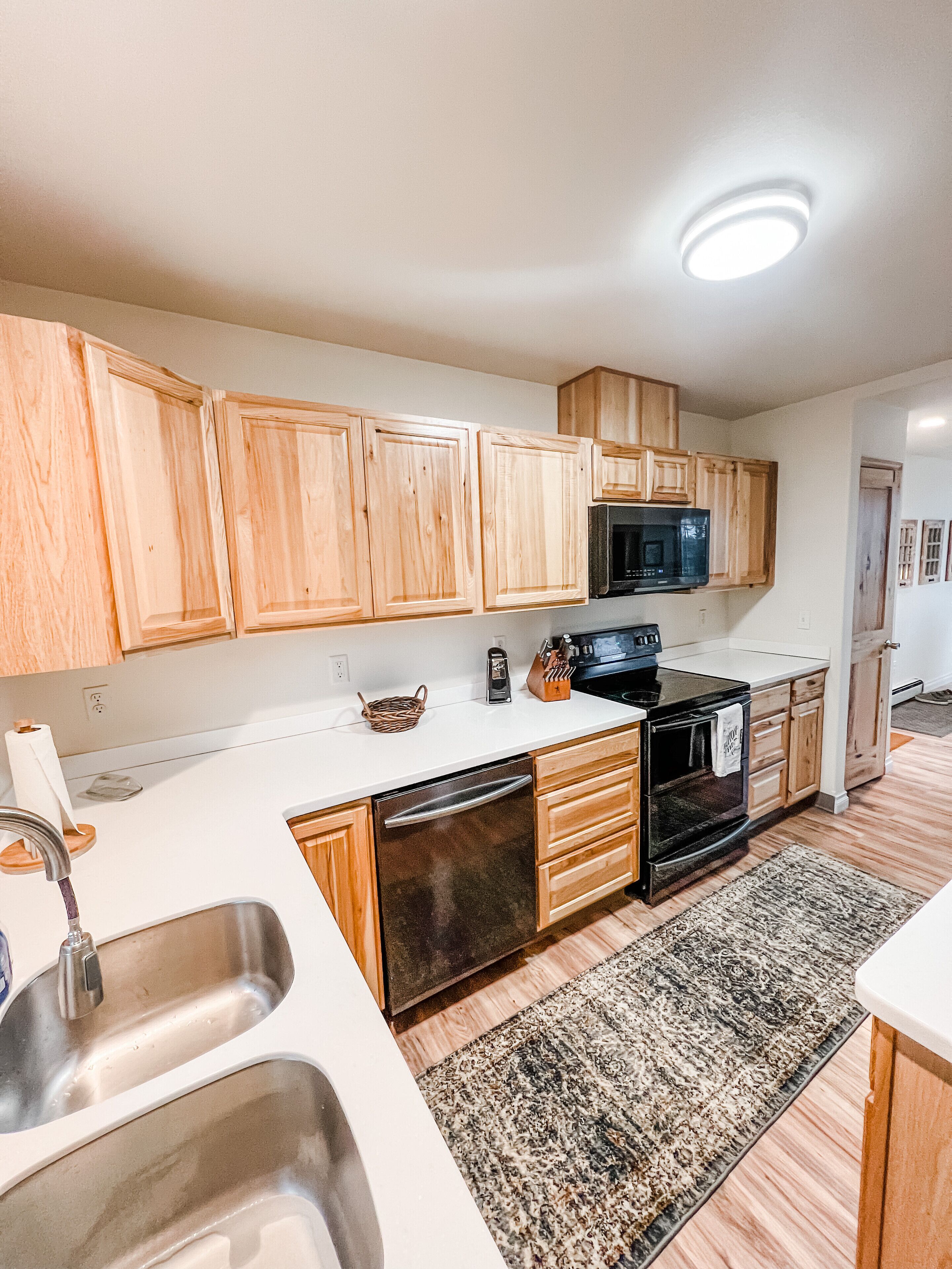 A modern kitchen with wooden cabinets, a stainless steel sink, a black dishwasher, and a microwave.