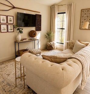 A cozy room with a large beige sofa, a small side table, a television, and a window with curtains.