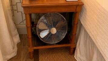 A wooden bedside table with a fan, a small potted plant, and a remote control.