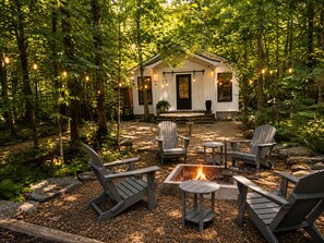 A cabin with a fire pit and Adirondack chairs in a forest setting. - secluded cottage- firepit, outdoor shower, hammock (Readyville)