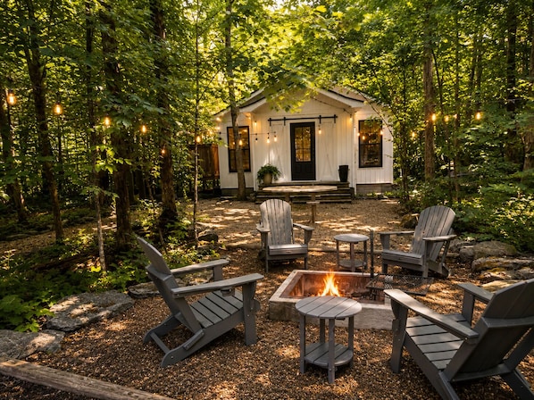 A cabin with a fire pit and Adirondack chairs in a forest setting.