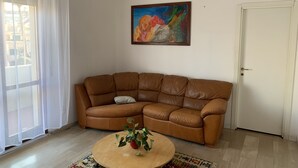 Un salón con un sofá de cuero marrón, una mesa redonda de centro con una planta, un cuadro abstracto de colores en la pared y una puerta blanca.