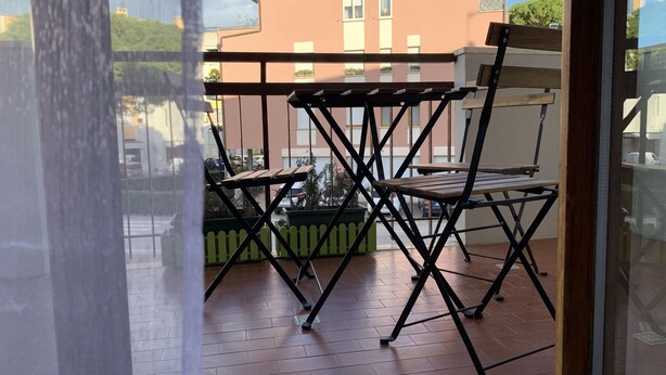 Un balcón con una mesa y sillas de madera, una maceta verde y vistas a edificios al fondo.