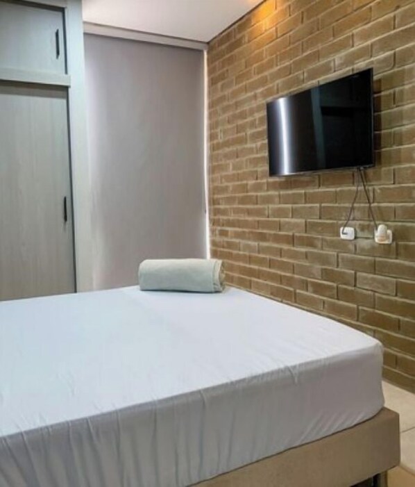 A bedroom with a bed, a TV mounted on a brick wall, and a wardrobe. - Live the best vacations in Cali, Colombia! (Cali)