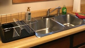 Una cocina con un lavamanos doble, un escurreplatos y un ventanal con vistas a árboles y flores.