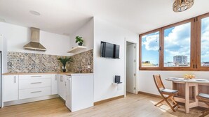 Ett modernt kök med vita skåp, kakel på väggen ovanför arbetsbänken och en matplats med ett träbord och stolar.