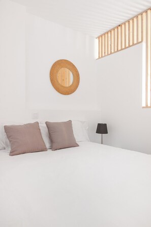 Une chambre à coucher au style minimaliste, avec un lit, deux oreillers, une lampe de chevet et une décoration murale en fibres tressées.