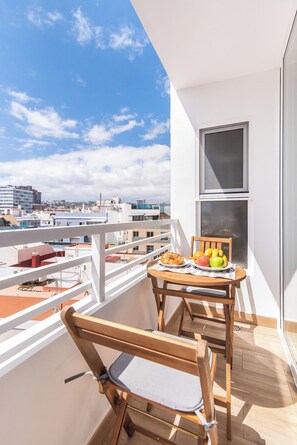 Un balcon avec une table dressée pour deux personnes, une chaise et une vue sur le paysage urbain.
