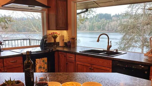 A kitchen with a large window overlooking a lake, wooden cabinets, and a stainless steel sink.