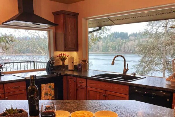 A kitchen with a large window overlooking a lake, wooden cabinets, and a stainless steel sink.