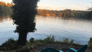 Two green Adirondack chairs facing a lake with a forested shoreline.