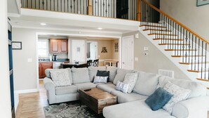 A spacious living area with a grey sectional sofa, a wooden coffee table, and a patterned rug. A staircase with wooden railings leads to an upper level. - Rest-Relax-Refresh (Waterloo)