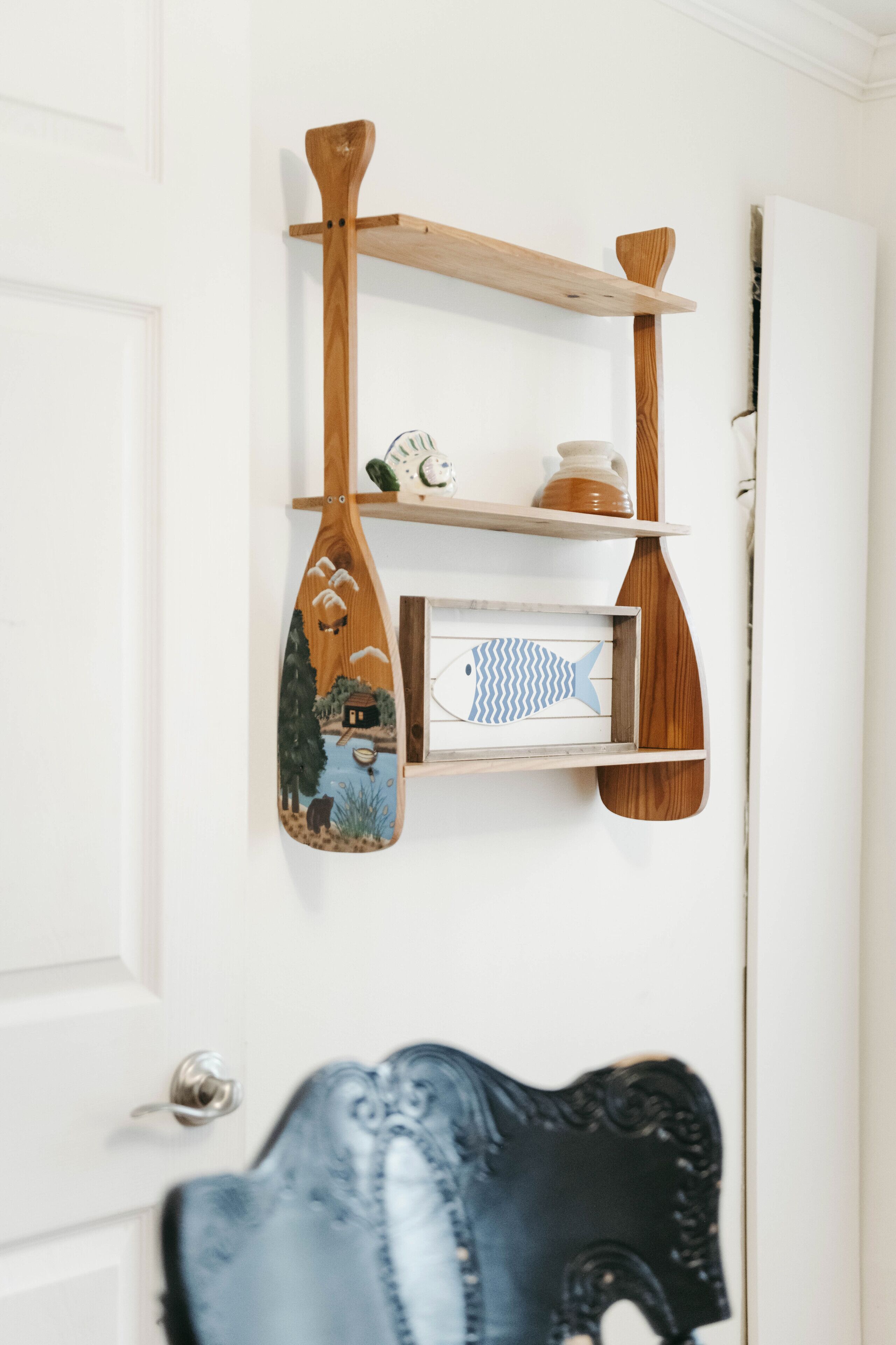 A wall-mounted wooden shelf with a painted fish and a small framed picture.