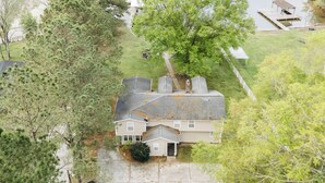 A two-story house with a large front yard, a dock extending into a lake, and a tree in the front yard. - Rest-Relax-Refresh (Waterloo)