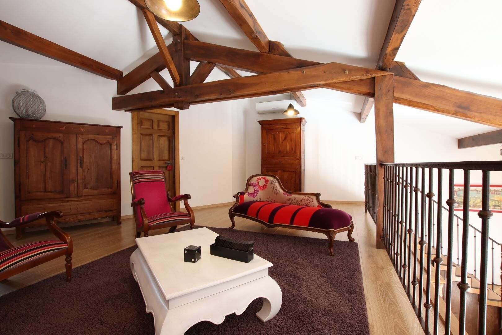 A spacious living room with exposed wooden beams, a red armchair, a sofa with a floral pattern, and a white coffee table.