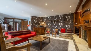 A cozy living room with a red sofa, wooden chairs, a coffee table, and a stone fireplace. - Martirenia - Osses - Gîte (OSSES)