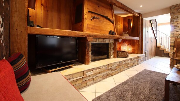 A spacious living area with a large flat-screen TV, a stone fireplace, wooden beams, and a staircase leading to another level. - Martirenia - Osses - Gîte (OSSES)