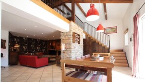 A spacious living area with a wooden dining table, a red sofa, and a stone fireplace. A staircase with wooden steps and a red pendant light is visible in the background. - Martirenia - Osses - Gîte (OSSES)
