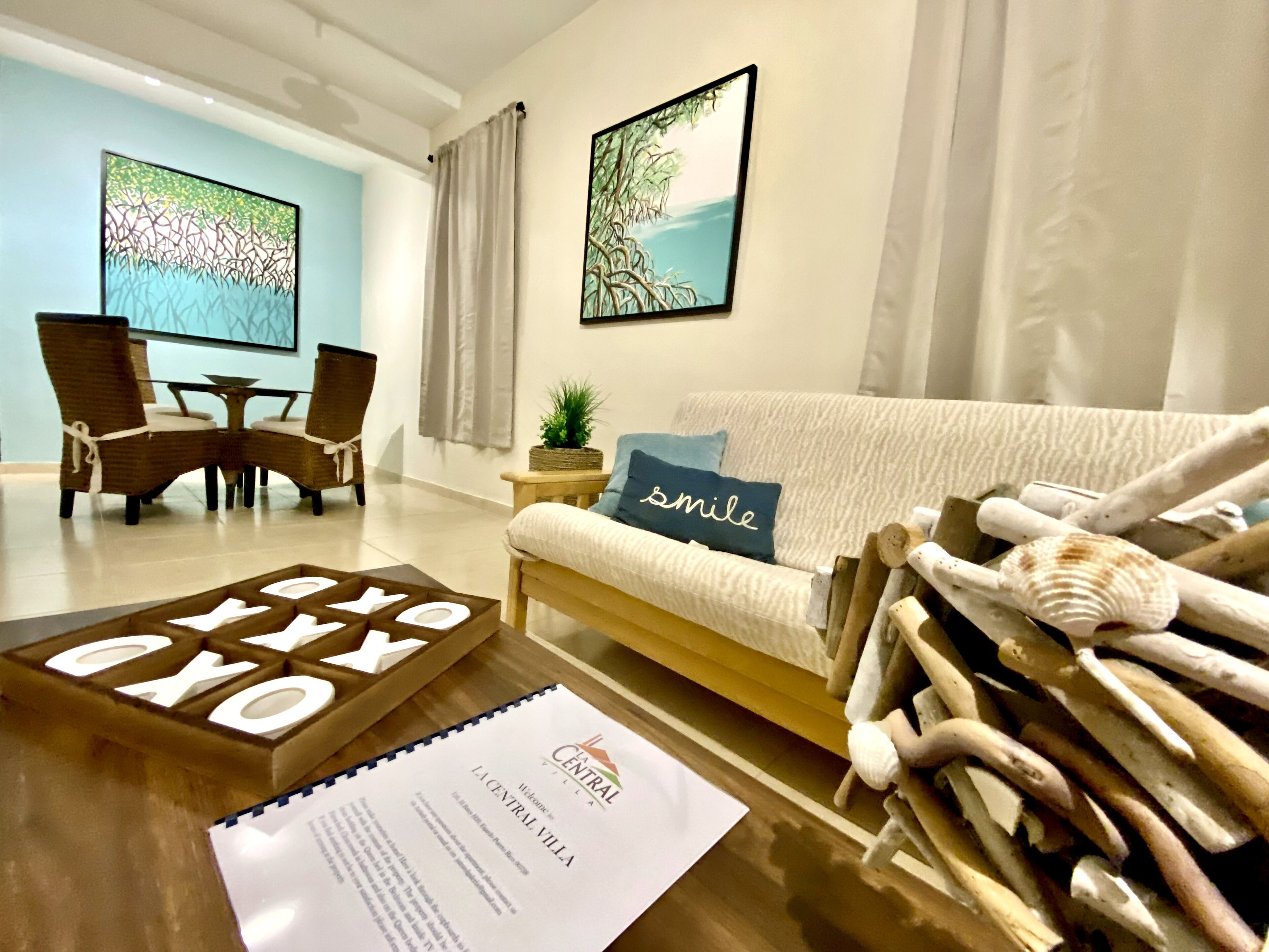 A modern living room with a sofa, a coffee table with a wooden sign, a small side table with a plant, and two framed artworks on the wall.
