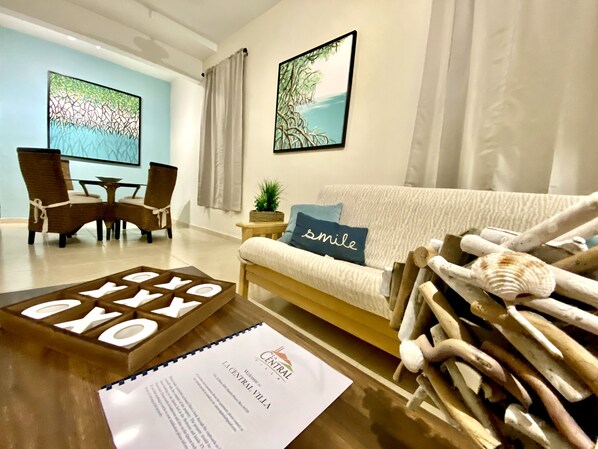 A modern living room with a sofa, a coffee table with a wooden sign, a small side table with a plant, and two framed artworks on the wall. - La Central Villa / Cozy, Private and Centric Stay Near Downtown Fajardo (Fajardo)