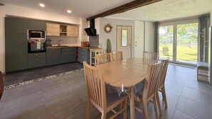 A modern kitchen with a dining area, large windows, and a view of the outdoors. - Gite DU Chene - Ledeuix (LEDEUIX)