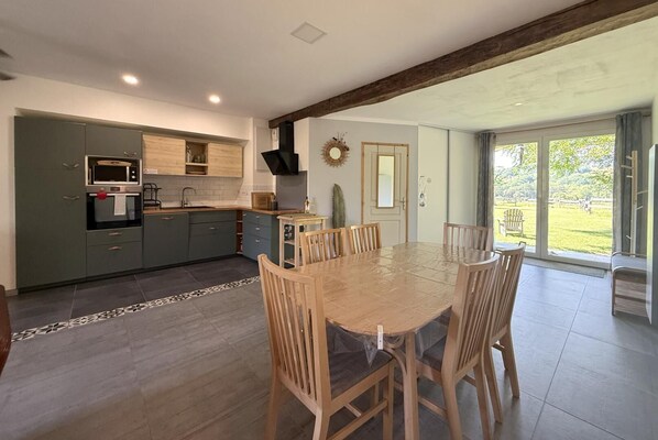 A modern kitchen with a dining area, large windows, and a view of the outdoors. - Gite DU Chene - Ledeuix (LEDEUIX)