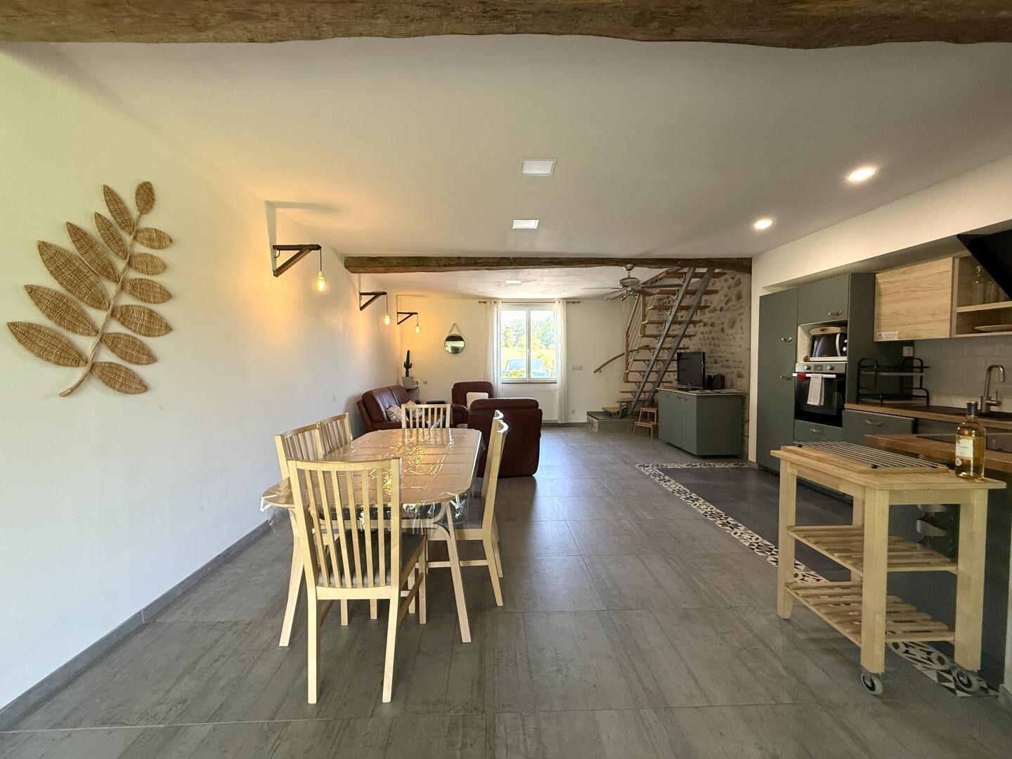 A spacious living area with a dining table, chairs, a sofa, a staircase, and a kitchen area.