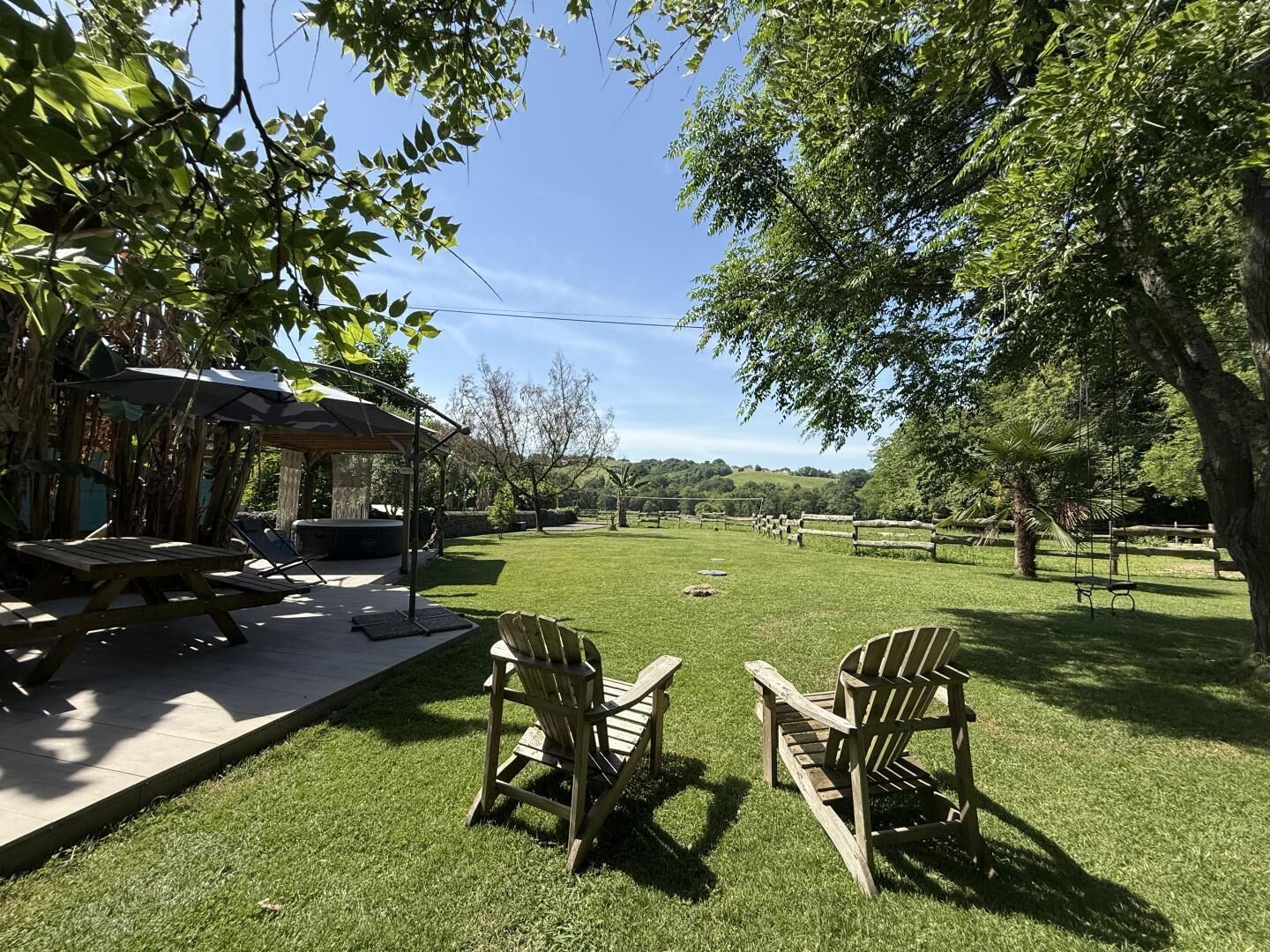 A patio area with a wooden table and chairs, a covered seating area, and a view of a grassy field with trees.