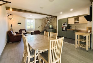 A dining area with a table and chairs, a kitchen with cabinets and appliances, and a staircase leading to an upper level. - Gite DU Chene - Ledeuix (LEDEUIX)